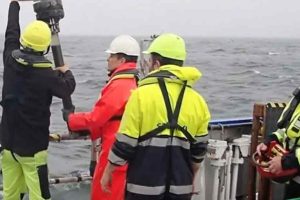 Forsker Kasper Urup Kjeldsen (rødt regntøj) hiver en boreprøve fra bunden af Aarhus Bugt ombord på forskningsskibet Aurora. I prøven gemmer sig mikroorganismer, som bærer rundt på en velbevaret hemmelighed. (Foto: Screendump fra video af Christof Pearce)