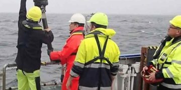 Forsker Kasper Urup Kjeldsen (rødt regntøj) hiver en boreprøve fra bunden af Aarhus Bugt ombord på forskningsskibet Aurora. I prøven gemmer sig mikroorganismer, som bærer rundt på en velbevaret hemmelighed. (Foto: Screendump fra video af Christof Pearce)