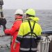 Forsker Kasper Urup Kjeldsen (rødt regntøj) hiver en boreprøve fra bunden af Aarhus Bugt ombord på forskningsskibet Aurora. I prøven gemmer sig mikroorganismer, som bærer rundt på en velbevaret hemmelighed. (Foto: Screendump fra video af Christof Pearce)